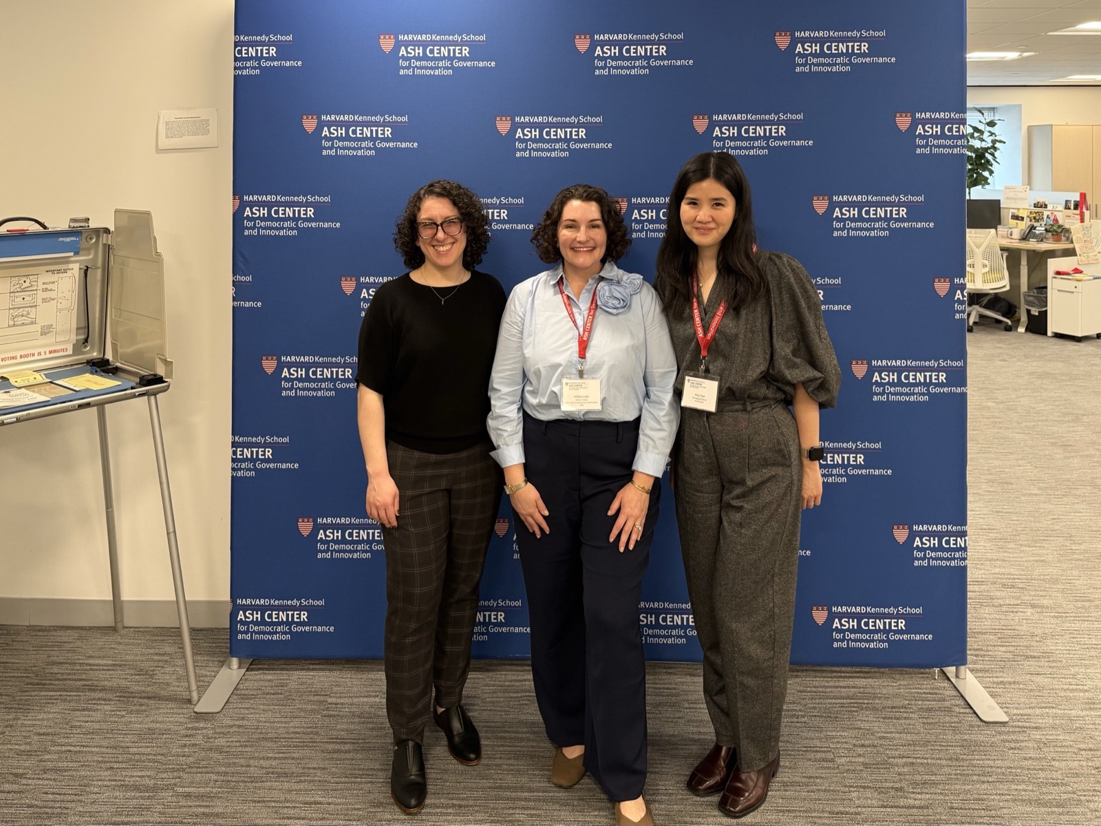 Emily Fishbaine, Hillary Lehr, and Anyi Sun standing together in front of an Ash Center backdrop at the Harvard Ash Center.